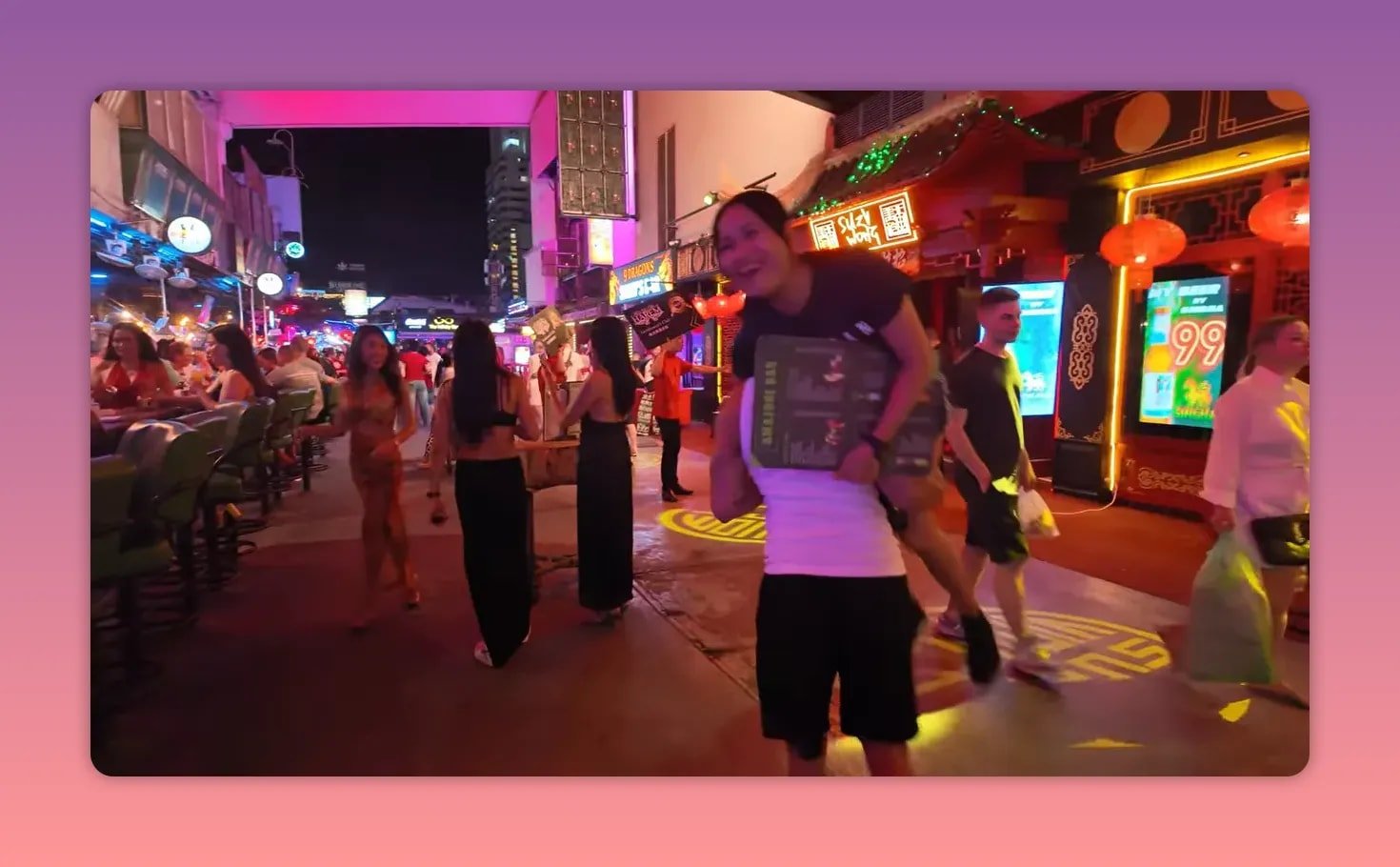 Rue nocturne bordée de bars avec lanternes rouges, enseignes lumineuses et passants