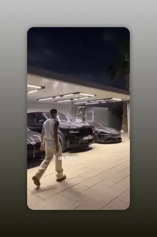 allée de garage éclairée avec plusieurs voitures de luxe noires et un homme qui marche devant