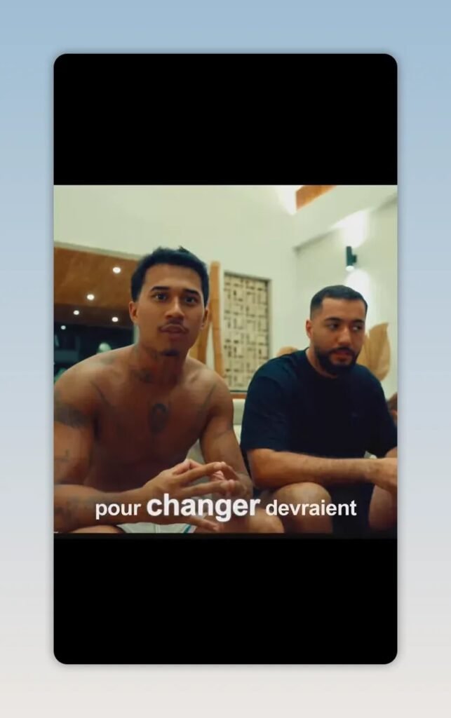 Deux hommes assis sur un canapé dans un salon, avec des sous-titres affichés en bas de l image