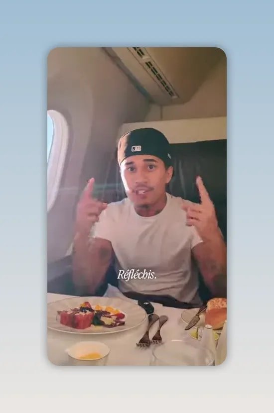 homme assis dans un avion qui pointe ses doigts vers sa tête au-dessus d'une table avec assiettes et nourriture